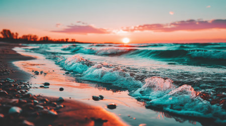 A scenic view of a winter sunset over the ocean, with colorful clouds and icy foam washing up on the wet, reflective sand of the shoreline.の素材