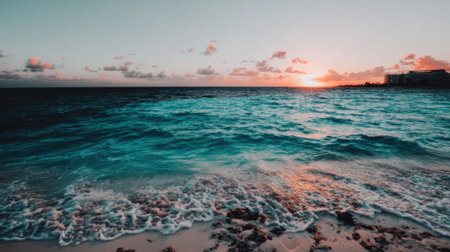 A breathtaking view of the ocean at dusk. The turquoise waves gently wash onto the shore as the sun sets on the horizon, casting a warm glow on the clouds and water.の素材