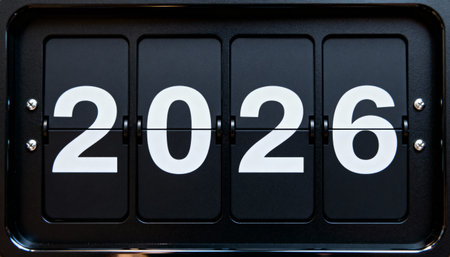 Close up of a black retro flip clock with white numbers. The mechanical scoreboard display shows the year 2026, symbolizing the future, time passing, and new beginnings.の素材
