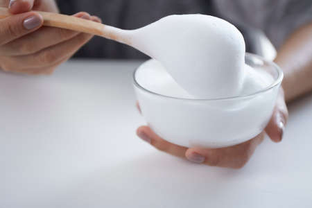White organic cosmetic foam in bowl with female hand holding wooden spoonの写真素材