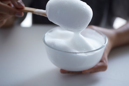White organic cosmetic foam in bowl with female hand holding wooden spoonの写真素材