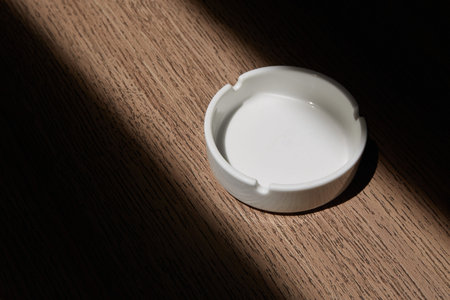 Ceramic ashtray on a wooden table with a shadowの写真素材