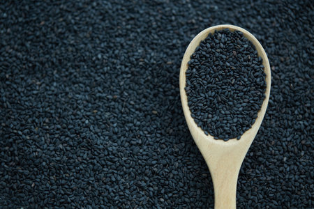 Black sesame seeds in wooden spoon on black background, top viewの写真素材