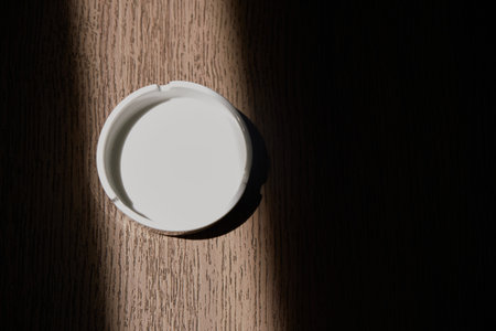 Top view of ceramic ashtray on a wooden table with a shadow