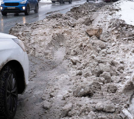 dirty snow on the side of the road prevents the exit of cars. the tractor has not completely removed the snowの写真素材