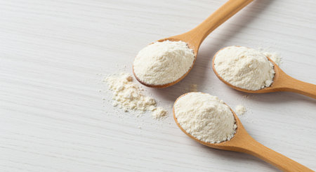 White wheat flour in wooden spoons on white wooden table background.の素材