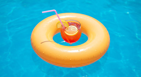 Orange cocktail with lemon and straw floating in swimming pool, summer vacation conceptの素材