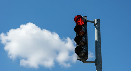 Traffic light with red signal on blue sky background with white cloudsの素材