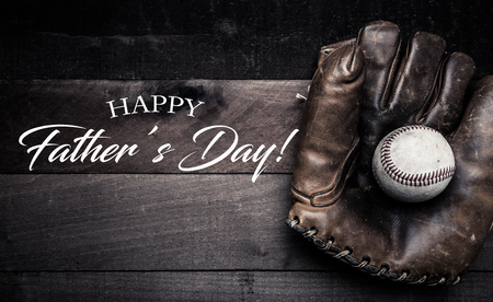 A group of vintage baseball equipment, bats, gloves, baseballs on wooden background with a fathers day greetingの写真素材