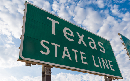 Texas state line road sign in front of cloudy skyの写真素材
