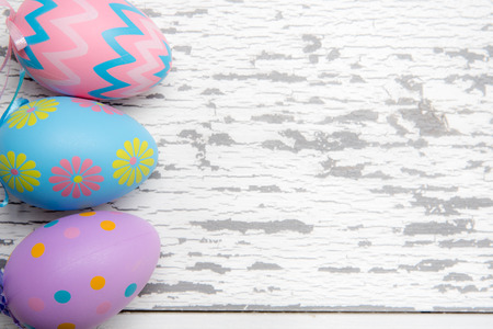 A group of pastel colored Easter eggs on a white, aged wooden background with copy space.の写真素材