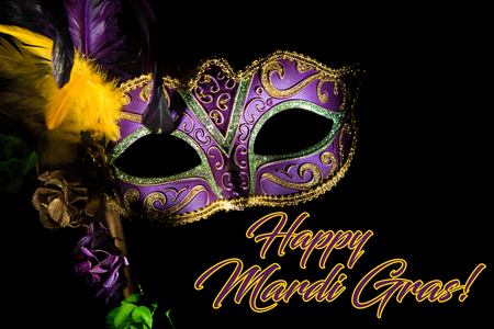 A purple mardi gras or venitian mask with feathers and flowers on a black background with copy spaceの写真素材