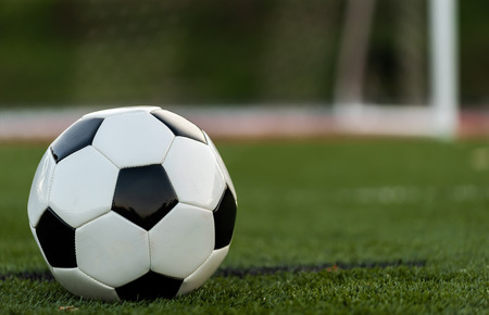 A black and white soccer or football on green field with goal or net in backgroundの写真素材