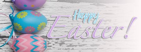 A group of pastel colored Easter eggs on a white, aged wooden background with greeting.の写真素材