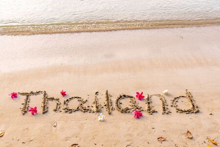the word thailand on sand, exotic frangipani flowers on the seashore, paradise flowers plumeria, background picture with flowers by the ocean, yellow sand in Asiaの写真素材