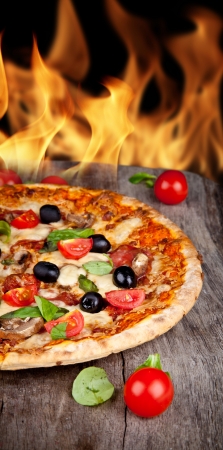 Delicious italian pizza served on wooden table with flames on backgroundの写真素材