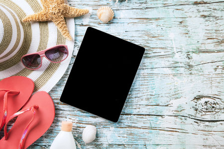 Top view of summer accessories and blank tablet on wooden planks