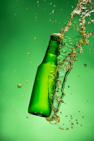 Bottle of beer with splash around on green backgroundの写真素材