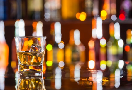 Whiskey drink on bar counter with blur botles on backgorundの写真素材