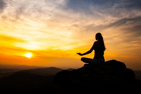 Yoga practicioner sitting on rock during the sunset meditationの写真素材