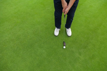 Golf player at the putting green. Hitting ball into a holeの写真素材