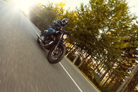 A young man riding a chopper on a road in morning sun