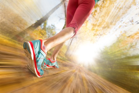 Close up of feet of female runner running in autumn leaves. Fitness exercise. Blur motion