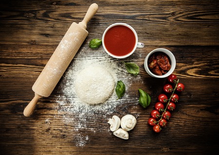 Pizza dough with ingredients on wood, shot from aboveの写真素材