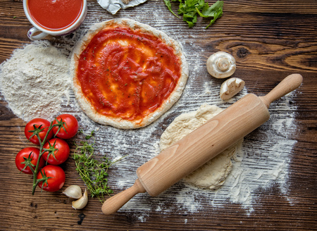 Pizza dough with tomato sauce on rustic wooden tableの写真素材