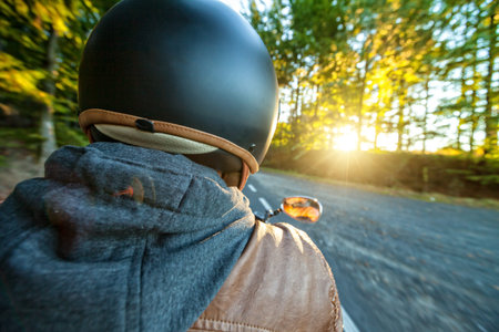 Motorcyclist riding motorbike  on road in morning sunny day. Shot from behind