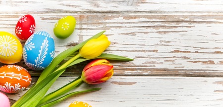 Colorful easter eggs and tulips placed on wooden backgroundの写真素材