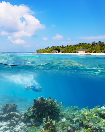 Young woman diver exploring coral reef under water surface. Tropical Maldives island resort on background, High resolutionの写真素材