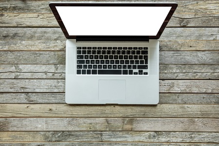 Modern designed laptop on old wooden desk. White screen for copyspaceの写真素材