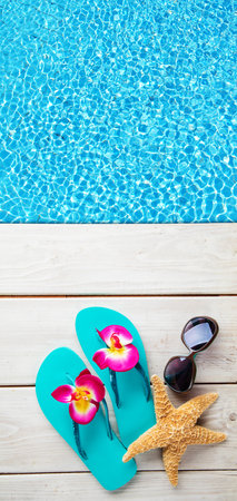 Beach accessories on wooden desk placed over swimming pool. Copyspace for text