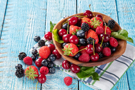 Fresh berry fruit pile in bowl with leaves placed on old wooden planksの写真素材