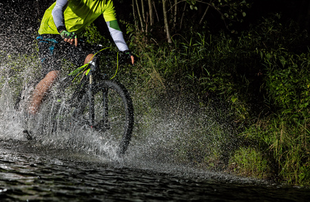 Mountain biker at night riding through forest stream and splashing water around. Close-up of side viewの写真素材