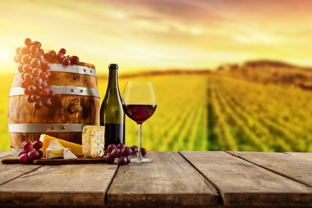 Red wine served on wooden planks with keg, vineyard on background, copyspace for textの写真素材