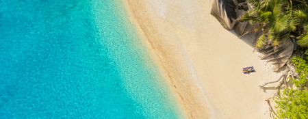 Aerial photo of beautiful sandy tropical beach with young woman sunbathing. Concept of summer travel vacation and relaxationの写真素材