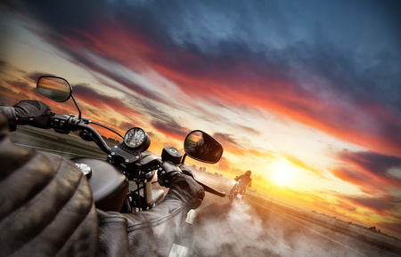 Motorbike riders driving towards cityscape panorama on empty asphalt motorway. Photographed from driver perspective. Beautiful sunset lightの写真素材