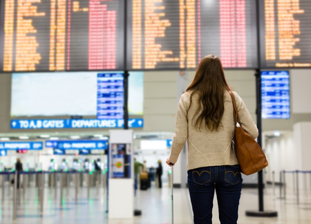 Young woman looking at the flight information board on the airport, checking her flightの写真素材
