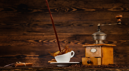 Splashing liquid of coffee into white cup placed on wooden table with grinder. Coffee beans falling aroundの写真素材