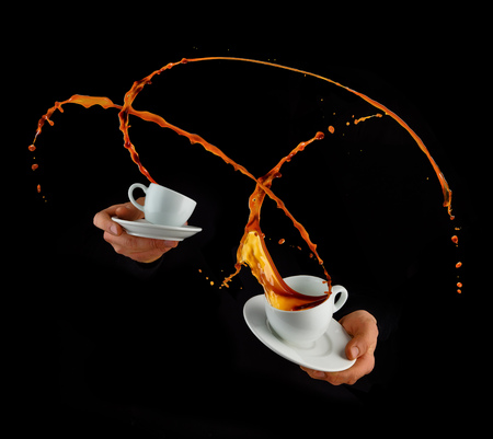 Man hands holding porcelaine cups with splashing liquid of coffee or tea, isolated on black backround. Hot drink with splashes, beverages and refreshment.の写真素材