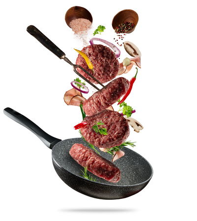 Flying raw milled hamburger meats pieces, with ingredients for cooking. Freeze motion of cooking staff and pan. Concept of food preparation in low gravity mode. Isolated on white backgroundの写真素材