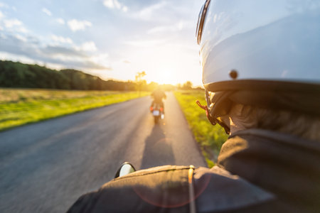 Motorbike riders driving towards beautiful sunset light on empty asphalt motorway. Photographed from driver perspective. Travel, freedom and transportation in outdoor natureの写真素材