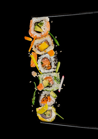 Sushi pieces placed between chopsticks, separated on black background. Popular sushi food.の写真素材