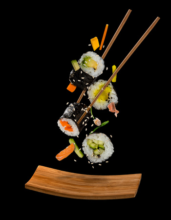 Sushi pieces placed between chopsticks, separated on black background. Popular sushi food. Very high resolution image