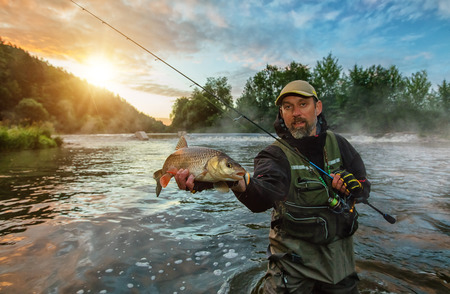 Sport fisherman holding trophy fish. Outdoor fishing in river during sunrise. Hunting and hobby sport.の写真素材