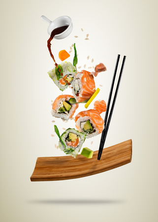 Flying sushi pieces served on wooden plate, separated on soft background. Many kinds of popular sushi food with chopsticks. Very high resolution imageの写真素材