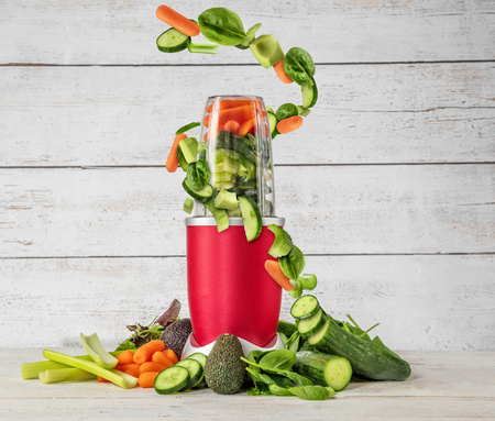 Smoothie maker mixer with vegetable flying ingredients, placed in wooden interior. Healthy drink and lifestyleの写真素材