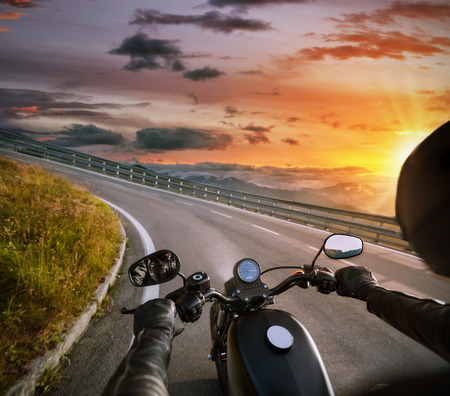 POV of motorbiker holding steering bar, riding in Alps in beautiful sunset dramatic sky. Travel and freedom, outdoor activitiesの写真素材